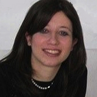 A woman with straight brown hair wearing a a black shirt and a pearl necklace